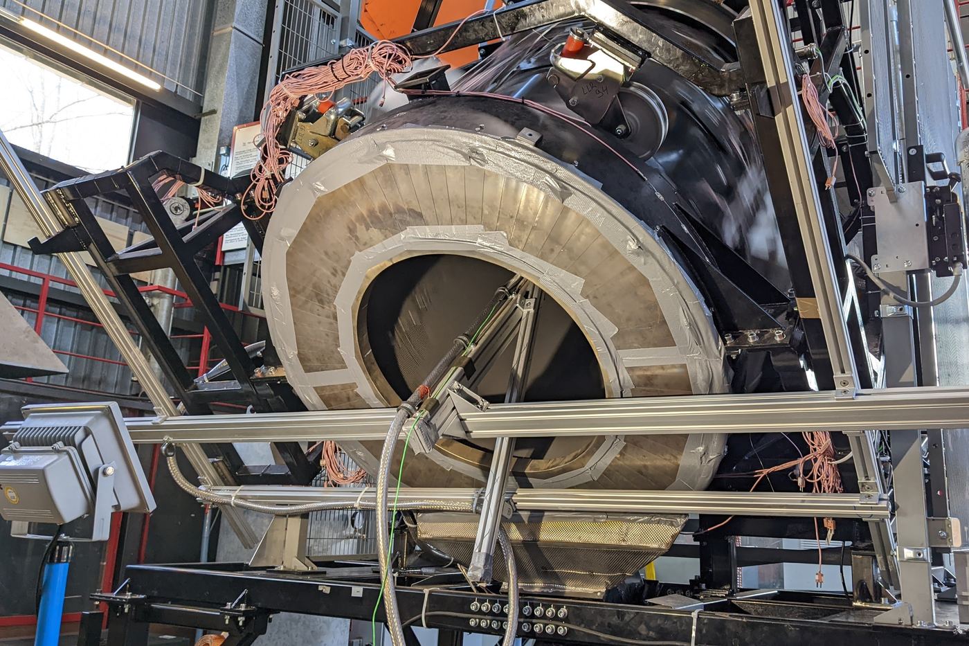 A large particle receiver with its circular opening, mounted in a test frame inside a high-bay building and wired with instrumentation